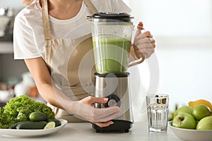 Woman preparing tasty green smoothie in kitchen