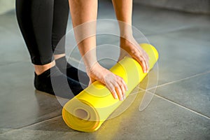Woman is preparing to unwrap yellow roll of sports mat for fitness. Hands lie on mat, close-up.