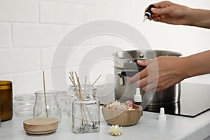 Woman preparing wax in kitchen, focus on jars with wicks and dry flowers. Making homemade candles