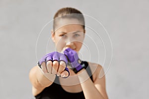 Woman preparing for workout at sport studio. Female in sportswear and fitness gloves standing isolated over gray studio background