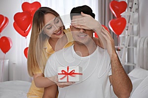 Woman presenting gift to her boyfriend in room decorated with heart shaped balloons. Valentine`s day celebration