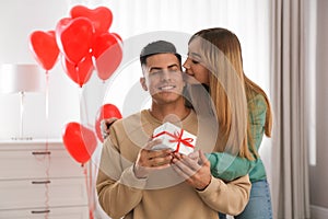 Woman presenting gift to her boyfriend in room decorated with heart shaped balloons. Valentine`s day celebration