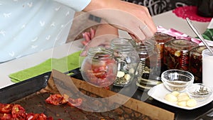 A woman preserves sun-dried tomatoes. Puts the ingredients in glass jars. The camera moves on a slider. Close-up