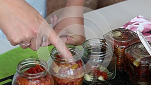 A woman preserves sun-dried tomatoes. Puts the ingredients in glass jars. The camera moves on a slider. Close-up