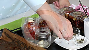 A woman preserves sun-dried tomatoes. Puts the ingredients in glass jars. The camera zooms in on the slider. Close-up