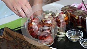 A woman preserves sun-dried tomatoes. Puts them in glass jars. The camera moves away on the slider. Close-up