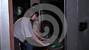 A woman presses buttons on an old control panel in a subway car, quest room.