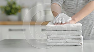 A woman presses down on a stack of folded white towels on a white table