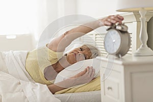 Woman Pressing Button Of Alarm Clock While Lying In Bed