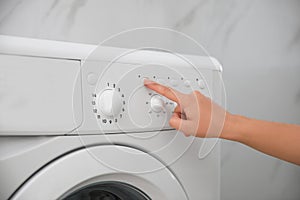 Woman pressing button on washing machine in bathroom, closeup