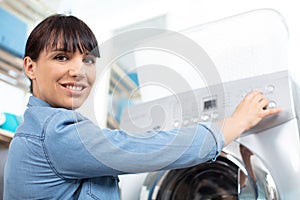 woman pressing button washing machine in kitchen