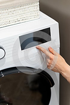 Woman pressing buttons on washing machine before doing laundry
