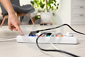 Woman pressing power button of extension cord on floor indoors. Electrician`s professional equipment