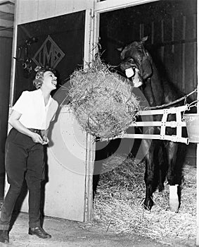 Woman pretending to eat hay bale with horse photo