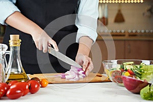 The woman in the process of making vegetable salad. Closeup of hands cutting red onions on wooden table