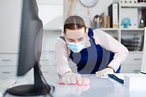 Woman professional cleaner in protective medical mask cleaning desk in office