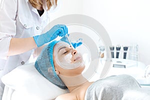 Woman professional doctor beautician applies a mask on a patient`s face for skin care. Cosmetic procedures for skin rejuvenation