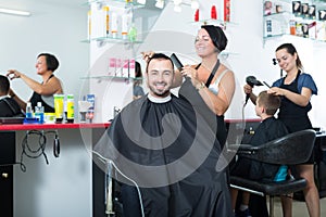 Woman professional hairdresser cutting male