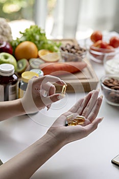 Woman professional nutritionist checking dietary supplements in hand, surrounded by a variety of fruits, nuts, vegetables