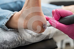 Woman on professional pedicure procedure by abrasive disc machine in beauty salon.