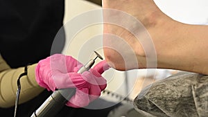 Woman on professional pedicure procedure by abrasive disc machine in beauty salon.