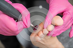 Woman on professional pedicure procedure by abrasive disc machine in beauty salon.