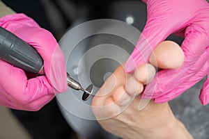 Woman on professional pedicure procedure by abrasive disc machine in beauty salon.