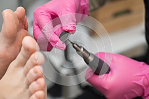 Woman on professional pedicure procedure by abrasive disc machine in beauty salon.