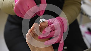 Woman on professional pedicure procedure by abrasive disc machine in beauty salon.