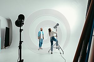 Woman professional photographer adjusts the light before shooting a man on a white background. Backstage