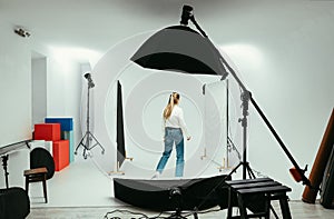 Woman professional photographer adjusts the light before shooting in a photo studio, rear view. Backstage