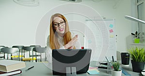 Woman professor sitting at table and lecturing online at class. Female English teacher in glasses speaking on tabletPC photo