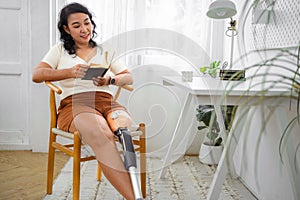 Woman with prosthetic leg reading book in room at home