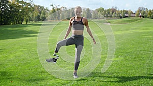 Woman with prosthetic leg warming in park. Girl exercising outdoors