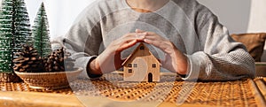 A woman protecting and covering wooden house model by hands with warmness