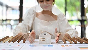 Woman protecting house model from falling wooden blocks with hands. Home insurance, risk and problem concept