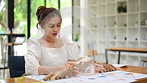 Woman protecting house model from falling wooden blocks. Home insurance, risk and problem concept