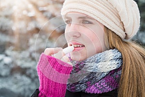 Woman protecting lips with lip balm on snowy day.