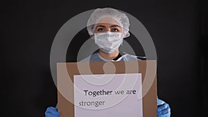 Woman in protective clothing holds a sign that reads NOWHERE TO RUN, TOGETHER WE WILL WIN, TOGETHER WE ARE STRONGER, WE