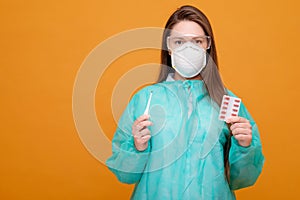 woman with protective equipment, thermometer and pills in hand in medical mask on yellow background, coronavirus pandemic, look at
