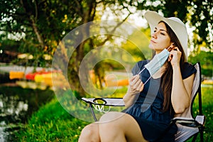 Woman with a protective face mask sitting in the park, spending time in nature. Mandatory mask wearing outdoors.Removing mask, end