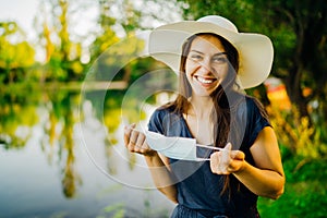 Woman with a protective face mask walking in the park, spending time in nature. Mandatory mask wearing outdoors.Removing mask, end