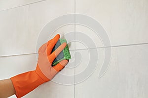 Woman in protective glove cleaning bathroom wall with sponge