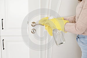 Woman in protective gloves disinfecting door handle while cleaning at home, close-up view on hands