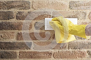 Woman in protective gloves disinfecting wall switches while cleaning at home, close-up view on hands