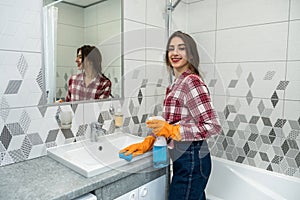 Woman in protective gloves holding a spray and a rag doing chores in bathroom, cleaning of water tap