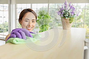 Woman in protective gloves is smiling and wiping dust on top shelf