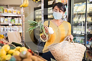 Woman in protective mask choosing greens in supermarket