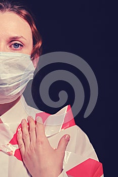 Woman in a protective mask on a dark background, half face. Close-up of a red-haired girl in a white shirt tied stop tape