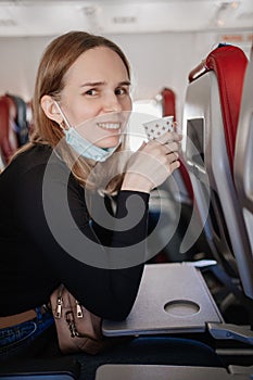 a woman in a protective mask drinks a drink from a paper cup on board the plane.